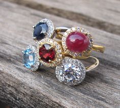 Halo Rings in Garnet, Blue Topaz, Blue Sapphire, Ruby. Create your Halo Ring with Belesas info@belesas.com Round Gemstones With Diamond Accents For Gifts, Diamond Ring With Gemstone Accents For Gift, Fine Jewelry Diamond Ring With Gemstone Accents, Diamond Ring With Gemstone Accents, Round Cut, Gift, Formal Round Birthstone Ring With Gemstone Accents, Ruby Crystal Ring With Accent Stones, Dazzling Round Gemstones With Diamond Accents, Dazzling Gemstones With Diamond Accents, Diamond Ring With Gemstone Accents As Gift