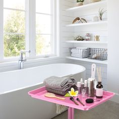 a pink tray with various items on it next to a bathtub in a white bathroom