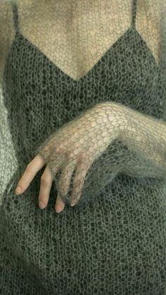 a woman with her hands on her chest wearing a green sweater and black lace gloves