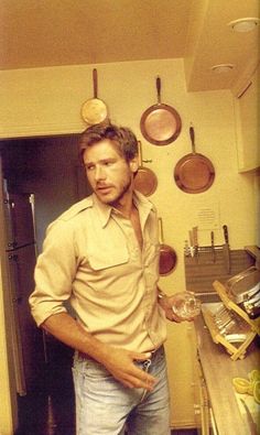 a man standing in a kitchen with pots and pans hanging on the wall behind him