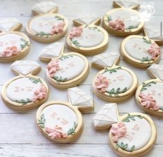 some decorated cookies are sitting on a white wooden table with pink flowers and leaves around them