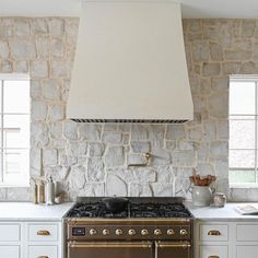 a stove top oven sitting inside of a kitchen next to a wall covered in stone