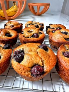 blueberry muffins cooling on a wire rack with bananas in the back ground