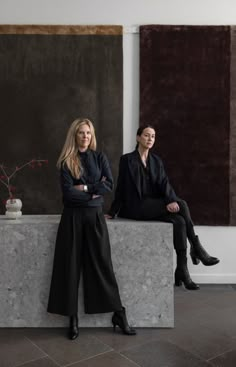 two women sitting on top of a stone bench