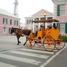 a horse drawn carriage on the street in front of some pink buildings with green shutters