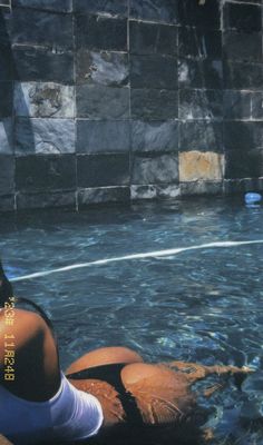 a woman sitting on the edge of a swimming pool with her feet in the water