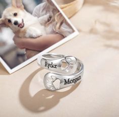 two silver rings with hearts and paw prints on them next to a photo of a woman holding a dog