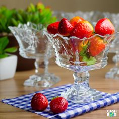 a glass bowl filled with strawberries on top of a blue and white checkered table cloth