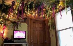 a tv sitting on top of a wooden table under a plant covered ceiling next to a window