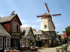 a windmill is in the background behind some shops and buildings with flowers on the sidewalk