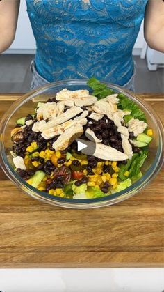 a woman standing in front of a glass bowl filled with chicken and black bean salad