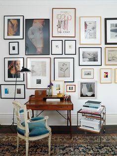 there is a desk and chair in the room with many pictures on the wall behind it