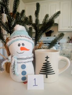 a knitted snowman sitting next to a coffee mug on a kitchen counter top