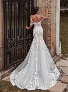 a woman standing in front of a gate wearing a wedding dress with an open back