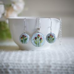 three earrings with flowers on them sitting in front of a white bowl and flower pot