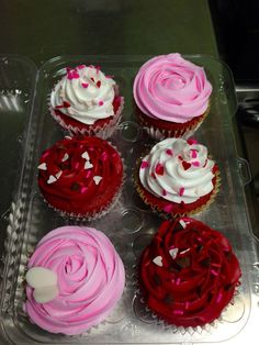 six cupcakes with pink and red frosting in a plastic container on a table