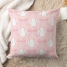 a pink pillow with baseballs and bows on it sitting on a fluffy rug next to a white towel