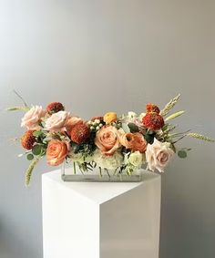 a white vase filled with lots of flowers on top of a wooden table next to a gray wall