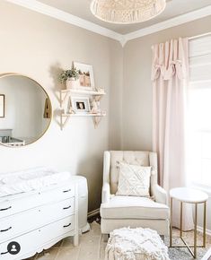 a baby's room with a white crib, pink curtains and a round mirror