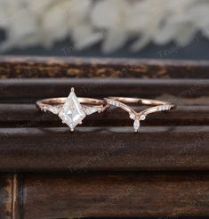 two gold rings with white diamonds on top and one diamond in the middle, sitting on a wooden surface