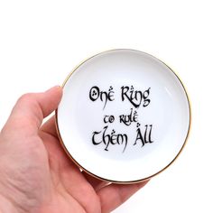 a hand holding a white and gold plate with the words, one kings go to ride them all