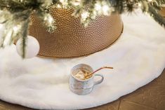 a cup of coffee sitting on top of a white rug next to a christmas tree