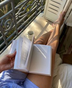 a woman is reading a book and holding a coffee cup on her lap while laying in bed