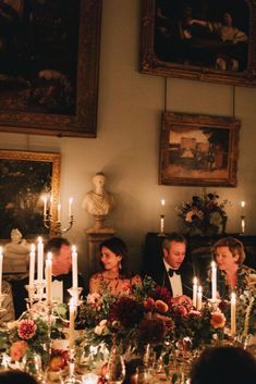 a group of people sitting around a table with candles in front of them and pictures on the wall