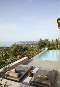 an outdoor lounge area next to a swimming pool overlooking the ocean and trees in the foreground