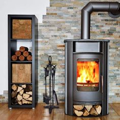 a wood burning stove sitting next to a stack of firewood on top of a hard wood floor