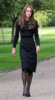 a woman in a black dress walking down a path