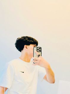 a young man taking a selfie with his cell phone while wearing a white t - shirt