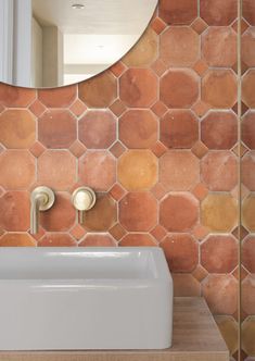 a bathroom sink sitting under a mirror next to a wall mounted faucet in front of a tiled wall