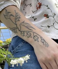 a woman with a tattoo on her arm holding a white flower in her left hand