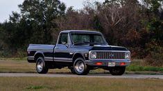 an old pickup truck is parked on the side of the road in front of some trees