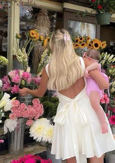 a woman holding a baby in her arms while standing next to flower shop filled with flowers