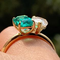 a woman's hand holding an emerald and diamond ring