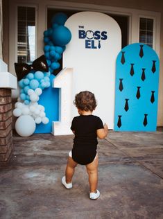 a small child standing in front of a blue and white balloon arch with the number one on it