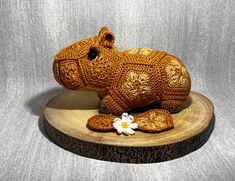 a crocheted hippo laying on top of a wooden stand with a flower in its mouth