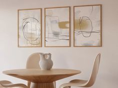 two paintings hang on the wall above a dining room table with chairs and a vase