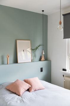 a bed with two pink pillows on top of it next to a wall mounted plant