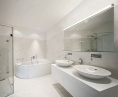 a white bathroom with two sinks and a bathtub in the middle, along with a large mirror