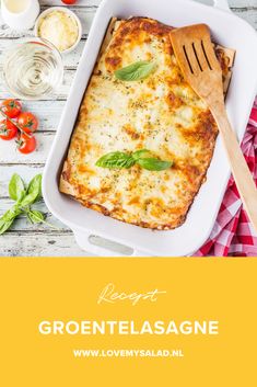 a white casserole dish with cheese and basil on the side next to a wooden spoon