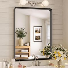 a bathroom sink sitting under a mirror next to a vase with flowers on top of it