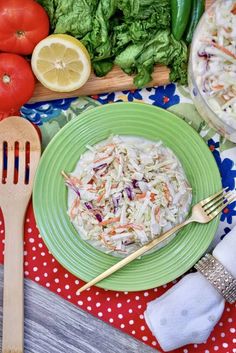 a green plate topped with coleslaw next to a salad and two wooden utensils