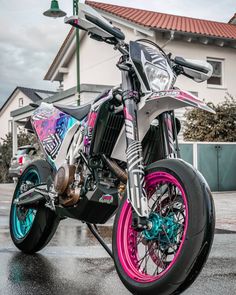 a pink and blue dirt bike parked in front of a building on a rainy day