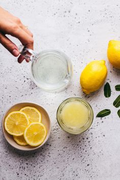 lemons, water and leaves sit on a table next to two bowls with lemonade in them