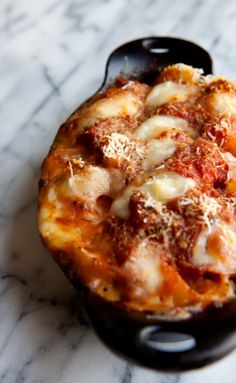 a small pizza sitting on top of a black pan covered in cheese and tomato sauce