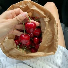 a person holding a paper bag full of cherries in their hand and sitting down