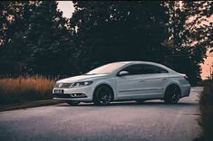 a white car is parked on the side of the road near some tall grass and trees